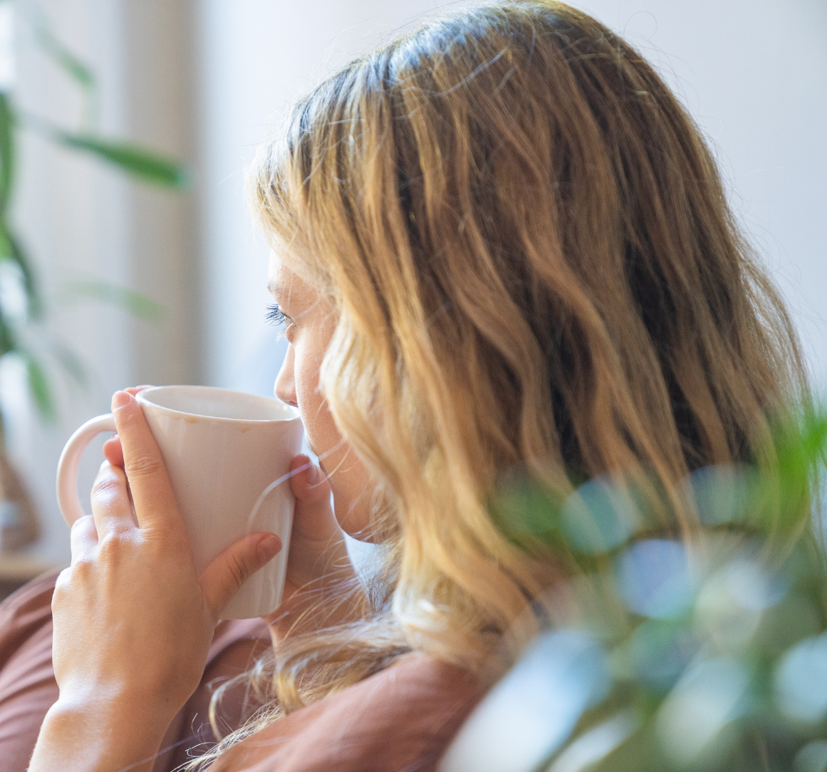Spravato Woman Coffee Relaxed woman sipping from a white mug in a sunlit room with plants—evoking calm, self-care, and the emotional healing supported by SPRAVATO treatment at Mind Rejuvenation.
