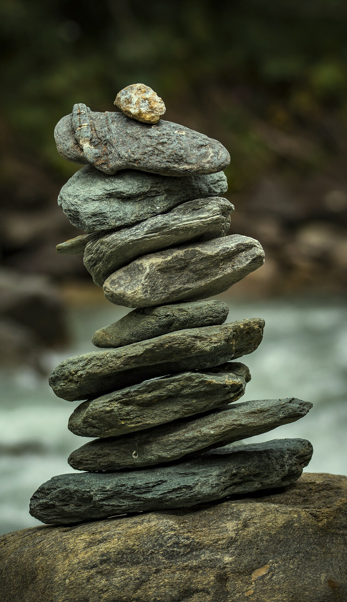 Stack of eleven smooth stones balanced vertically on a larger rock near flowing water, symbolizing mindfulness and stability. Featured on the Mind Rejuvenation About page in the What to Expect section to reflect balance, intentional care, and the art of healing.