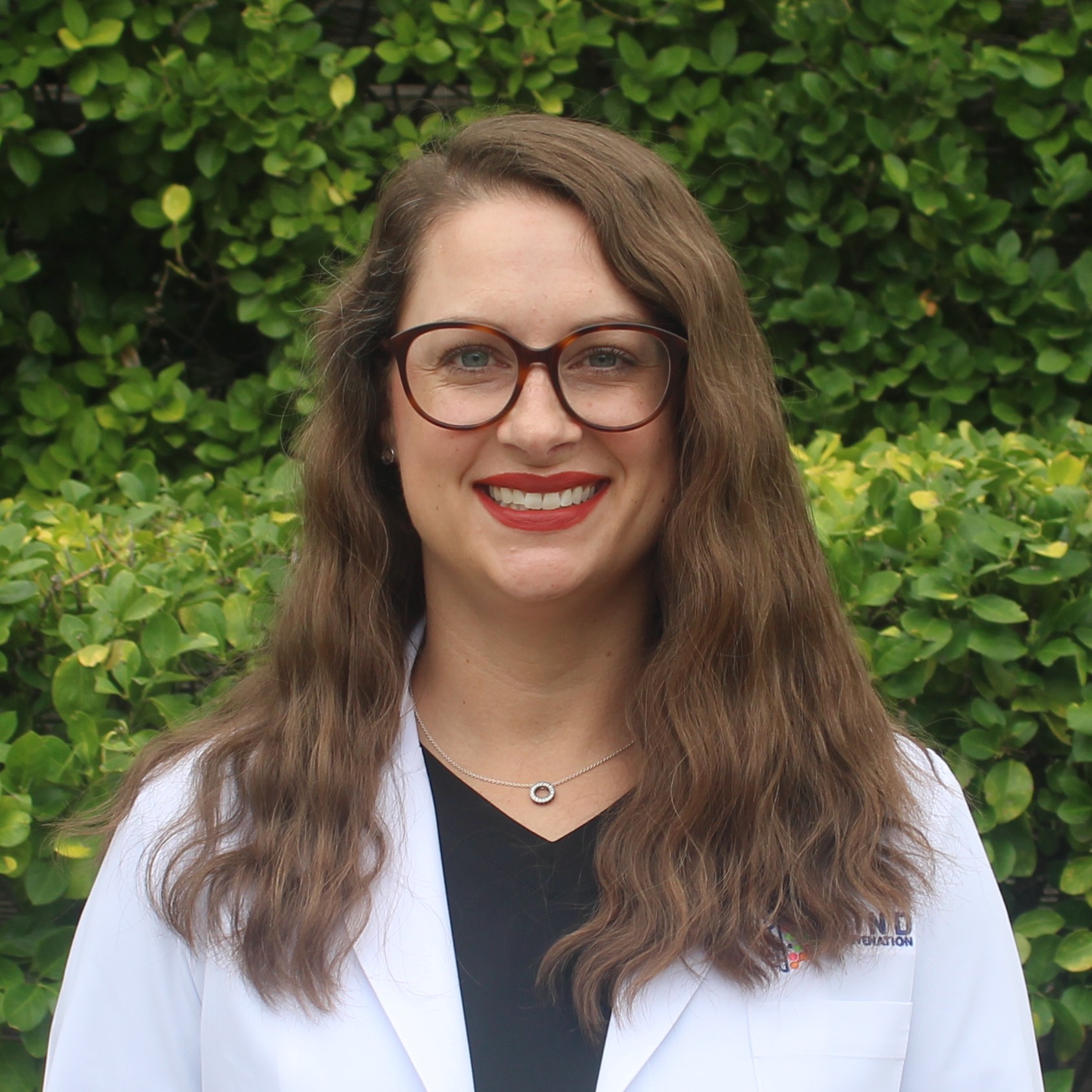 Nurse Practitioner Sarah Dorsey, APRN-CNP, FNP-C, smiling in a white lab coat outdoors against a green hedge. Featured on the Meet Our Team page to reflect compassionate care, clinical expertise, and a welcoming presence at Mind Rejuvenation.