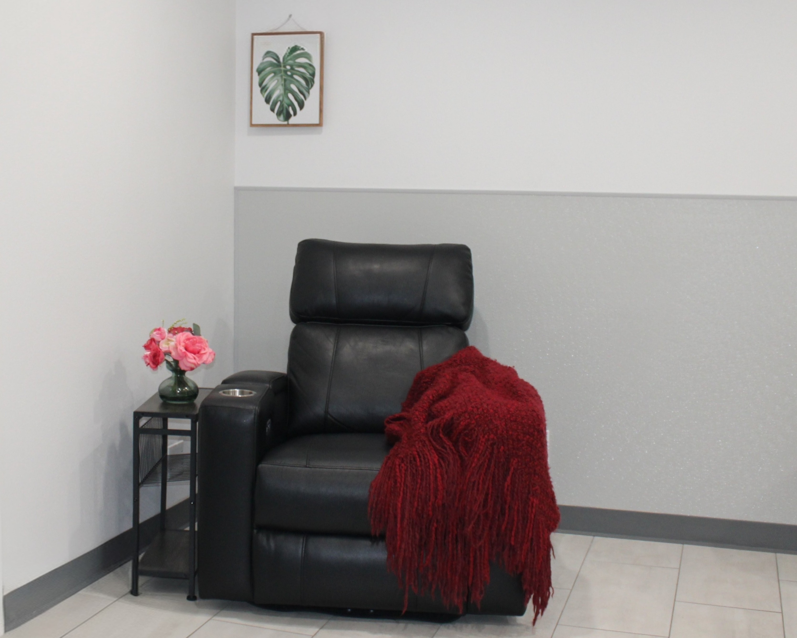Treatment Chair Cozy room corner with a black leather recliner draped in a deep red throw, beside a side table with pink and red flowers. Featured on the Mind Rejuvenation Home page to evoke comfort, calm, and a welcoming space for mental wellness.